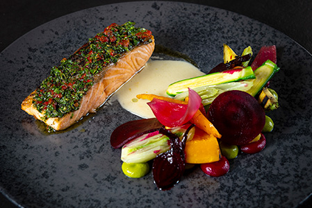 Ein Teller mit Lachs mit Kräuterkruste, Gemüsemischung und Sauce